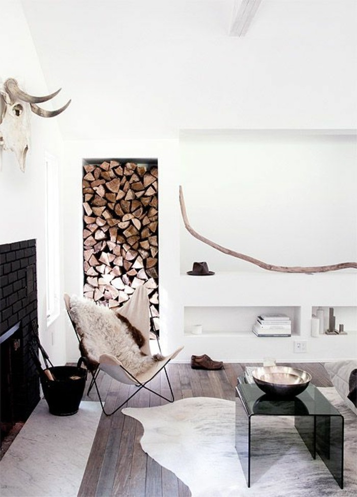 skull of an animal with horns, mounted on a white wall, above a black fireplace, inside a minimalistic, nordic style room, firewood and animal skins