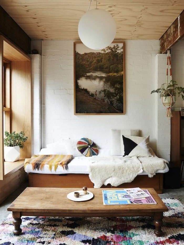 multicolored textured rug, inside a small living room, wooden settee covered in throws and blankets, simple living room designs, low vintage coffee table