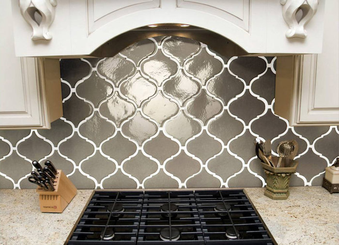 glossy creamy grey arabesque tile backsplash, with white joints, near a spotty beige counter top, with an inbuilt black hob