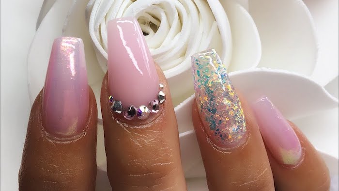 pearly sheen and iridescent glitter, in pale blue and pink, and several rhinestones, on the coffin nails of a hand, with four visible fingers
