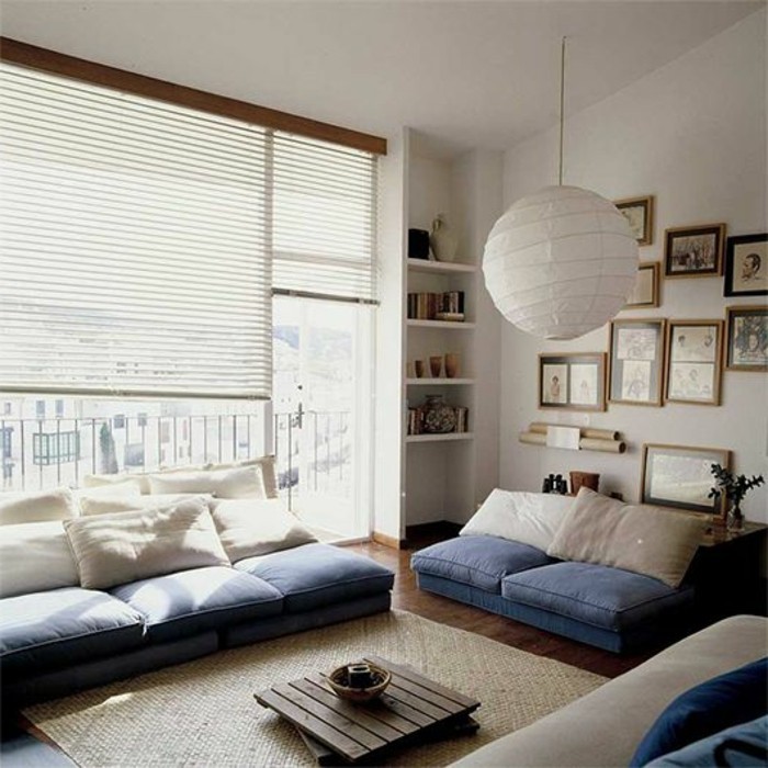 ground level sofa, and matching settee, made from blue and white cushions, placed on the floor, small wooden coffee table, large window with blinds