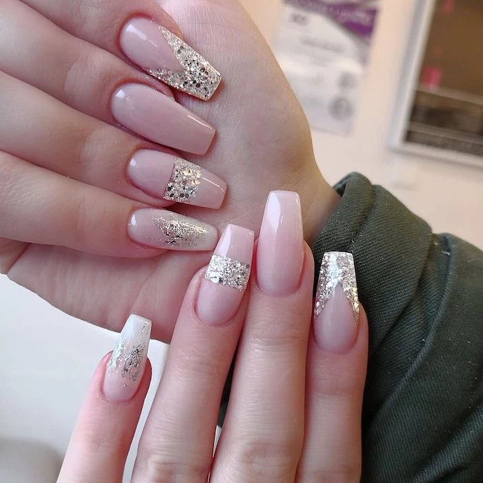 smudges and stripes, and geometric figures, created with silver glitter, decorating the baby pink manicure of two hands, coffin shaped nails