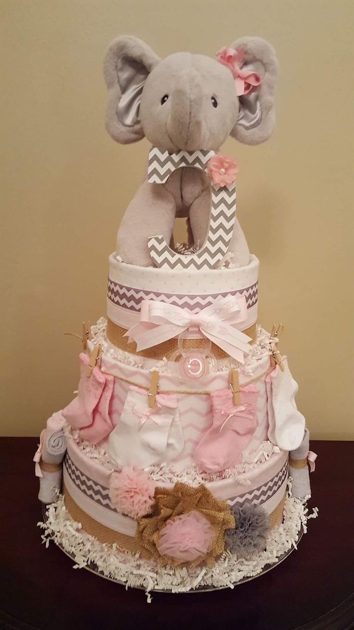 beige stuffed elephant toy, placed on top of a nappy cake, decorated with pale pink ribbons, little socks and tulle bows