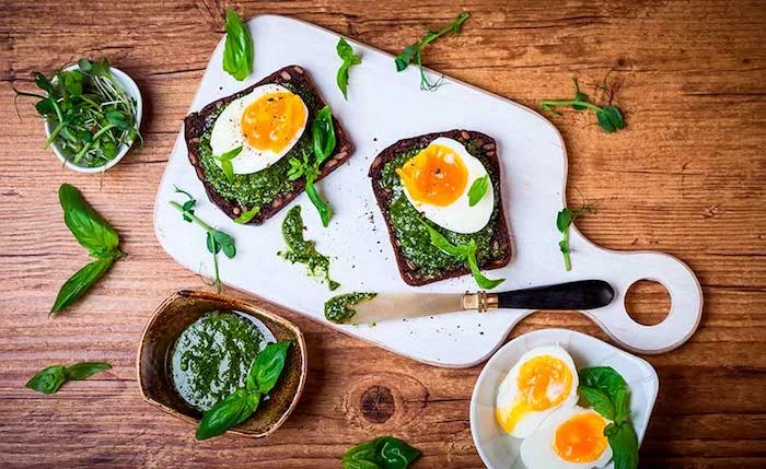 spread made from spinach, on two pieces of toasted bread, garnished with halves of boiled egg, and placed on a white cutting board