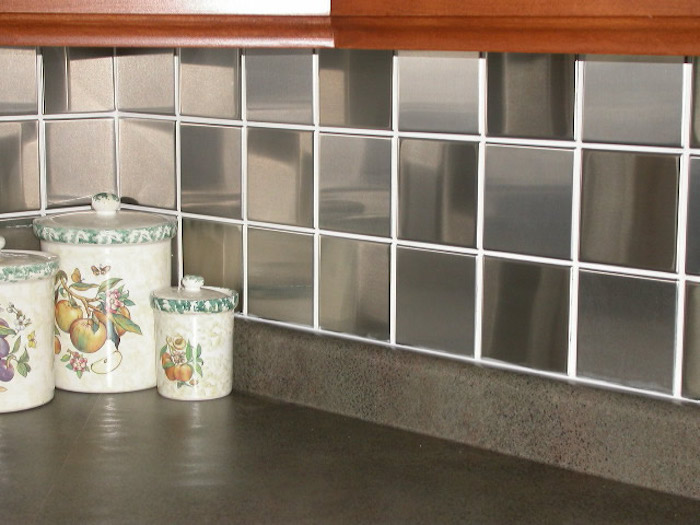 corner of a kitchen, covered in glossy and reflective, square dark grey tiles, with white joints, smooth dark grey counter top, with three colorful containers 