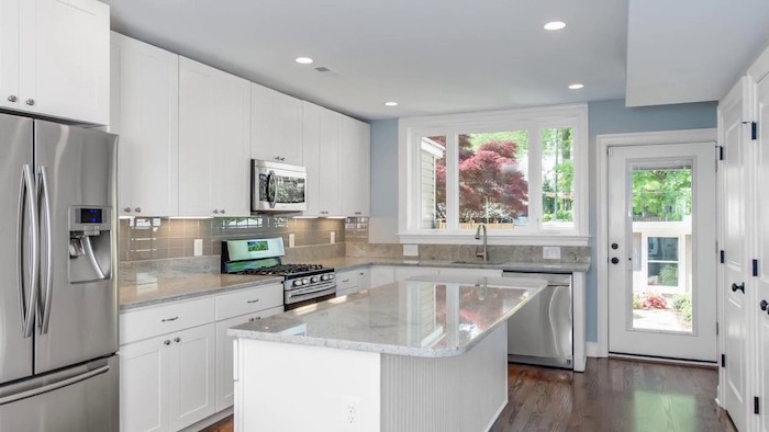 fridge in a metallic silver color, near a beige subway tile kitchen backsplash, white cabinets and glossy, marble counter tops