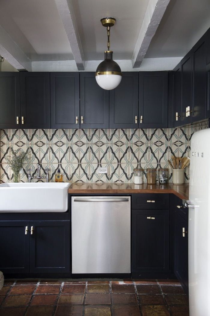 patterned tiles in cream, grey and pale blue, arabesque backsplash design, on the walls of a kitchen, with dark brown, natural stone floor, and black cabinets