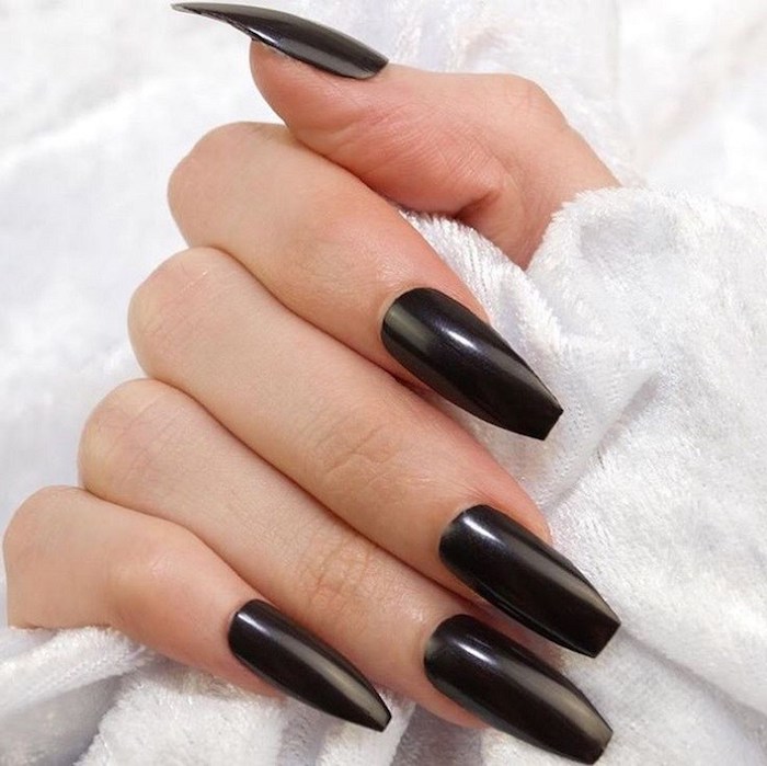 jet black smooth and shiny nail polish, on the long coffin nails, of a hand with folded fingers, holding a white, towel-like fabric