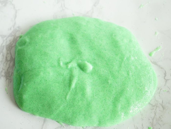 foamy green goop, flattened on a white and light grey, marble patterned surface, how to make slime without borax, soft and fluffy mixture