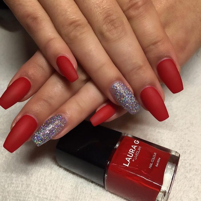 red matte nail polish, on medium long oval-shaped nails, with square tips, attached to a pair of tan hands, resting near a bottle of red nail polish