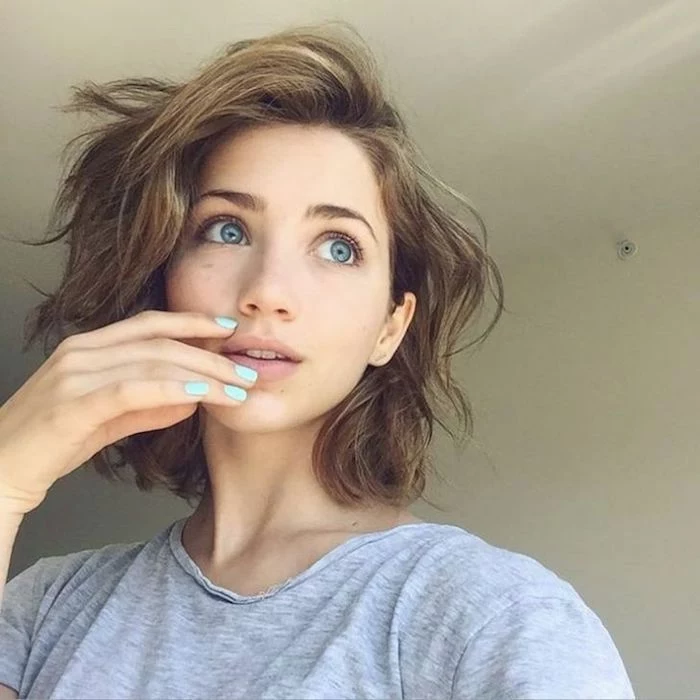 feathery and wavy, chestnut brown hair, with highlights and bangs swept to one side, on young girl with blue eyes, wearing a light grey t-shirt, short sassy haircuts 