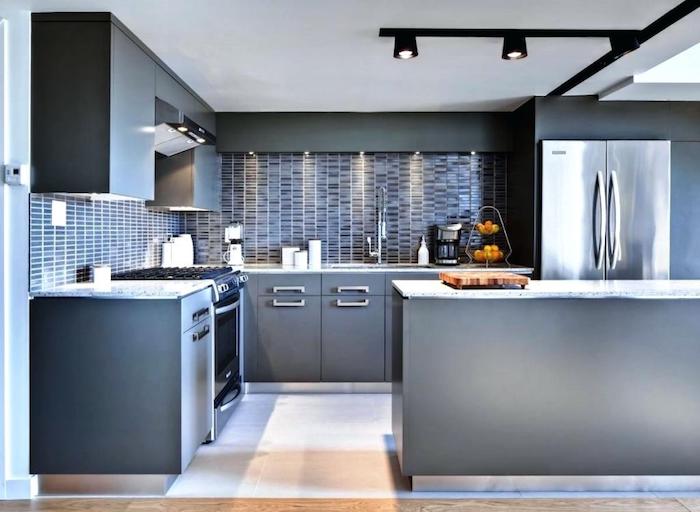 modern kitchen with grey cabinets, metal fridge and a light floor, walls covered with a bluish-grey subway tile pattern