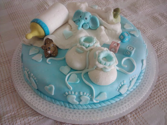 socks for a baby and a white blanket, baby bottle and toys, made from fondant, and topping a round, pale blue cake