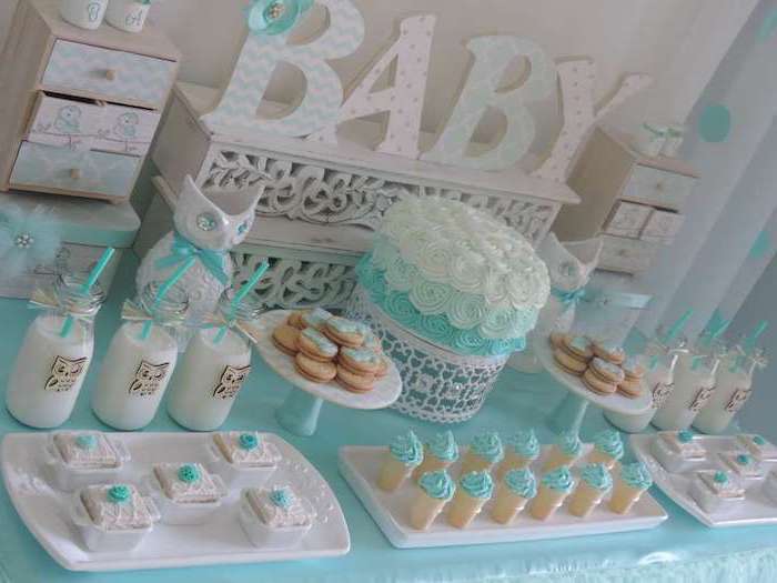 pastries and biscuits, decorated with pale turquoise, and white frosting, bottles with milk and turquoise straws, and a cake in the same colors, on a decorated table, with the word baby in large letters