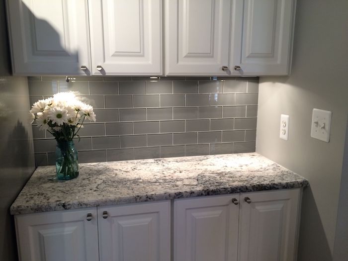 flowers in white, inside a clear blue, mason jar vase, placed on a grey and cream patterned counter, near a grey subway tile back splash