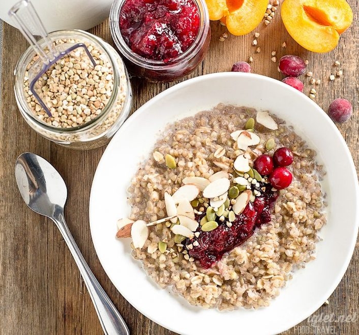 halved apricots and fresh cranberries, near a jar of cranberry sauce, and a jar with buckwheat, low calorie breakfast, bowl with porridge, topped with nuts and cranberries