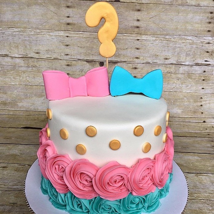 question mark cake topper in gold, placed over two fondant bows, one pink and the other blue, on a white cake, with gold buttons, and pink and teal roses, made from frosting