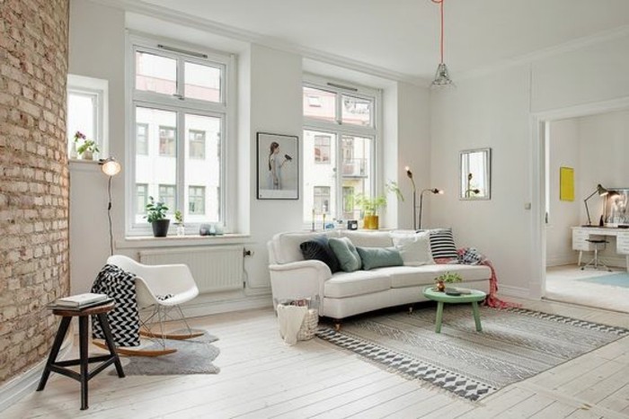 nordic style living room in white, with a brick wall accent, containing a white sofa, with several cushions, a patterned rug in grey, chairs and a turquoise coffee table, room setup ideas