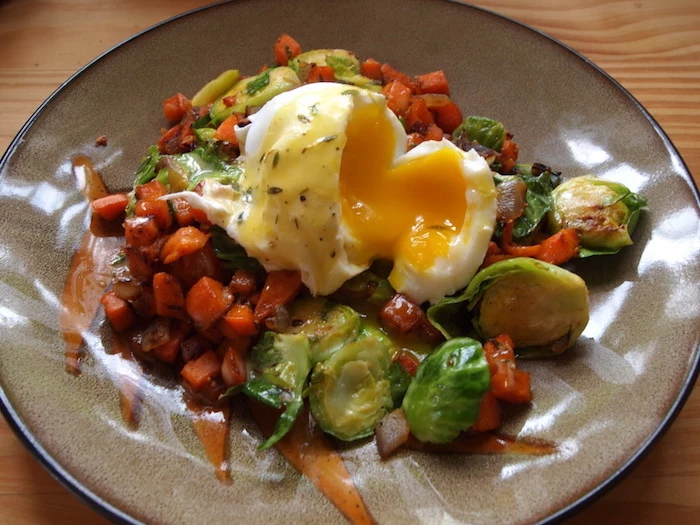 boiled egg cut open and runny, on a bed of cooked vegetables, breakfast menu ideas, Brussels sprouts and carrots, peppers and others