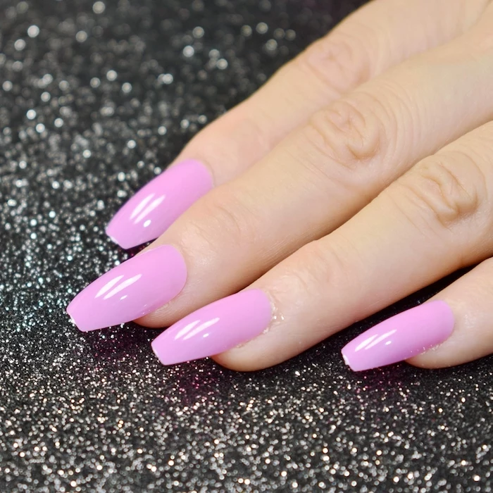 blush pink nail polish, on a hand with four visible coffin shaped nails, resting on a black surface, with silver glitter