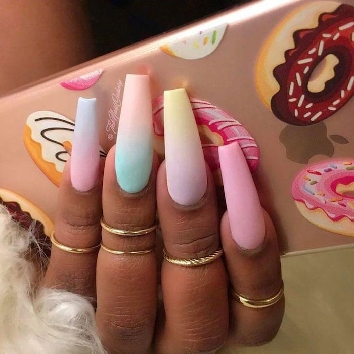 soft and light pastel colors, on four long nails, oval with square tips, attached to a dark brown hand, with five thin gold rings