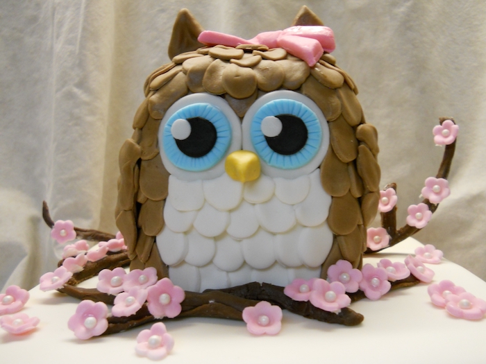 beige and white owl, with large blue eyes, made from fondant, owl baby shower cake, on a few brown fondant branches, decorated with pink cherry blossoms