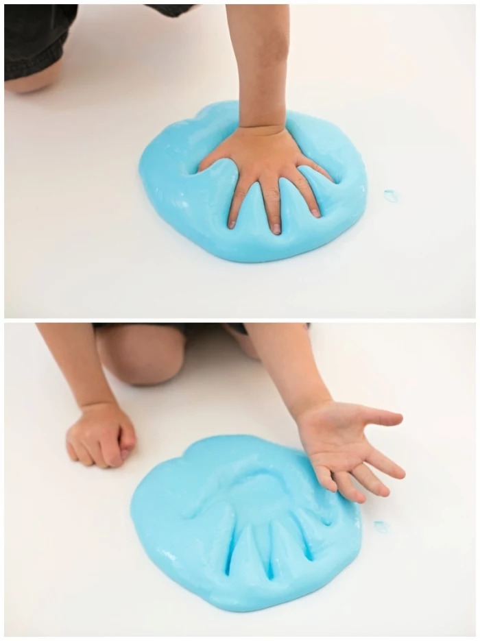small child pressing his or ehr hand, into a large pile of blue, fluffy slime, placed on a smooth, white surface or floor