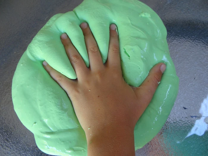 kid pressing his or her hand, on a pile of soft, foamy and gooey substance, how to make slime without borax, placed on a glass surface 