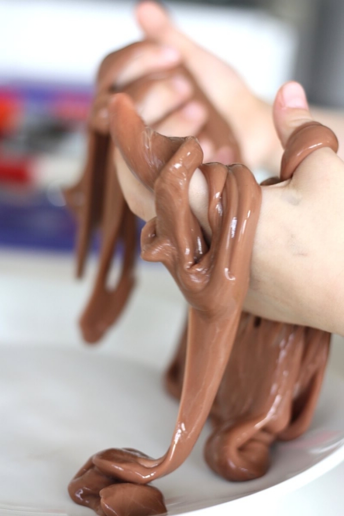 brown slimy goo, held over a white plate, by two small hands, how to make slime with borax, chocolate-colored stretchy slime 