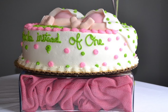 lime green and pink frosting, on a white round cake, decorated with a set of baby legs, in pink nappies, covered in white blanket, with green polka dots