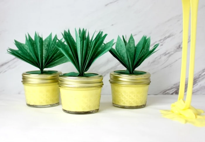 pineapples made from small jars, with green paper leaves, stuck to their lids, all jars are filled with yellow goo, how to make slime with glue, more yellow goo nearby