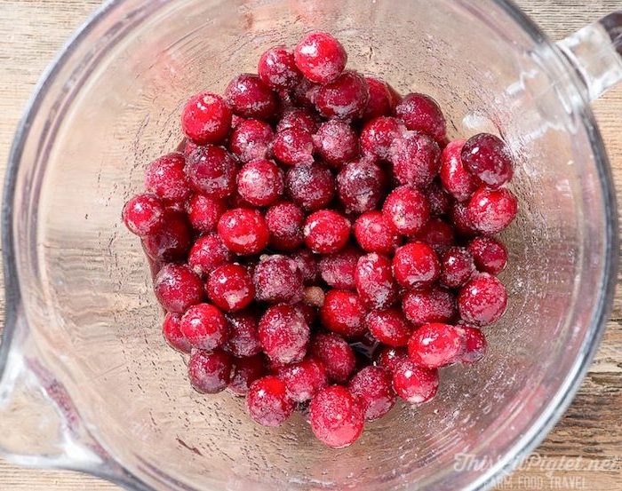 low calorie breakfast, cranberries dusted with sugar, inside a clear glass jug, with a handle, placed on a wooden surface