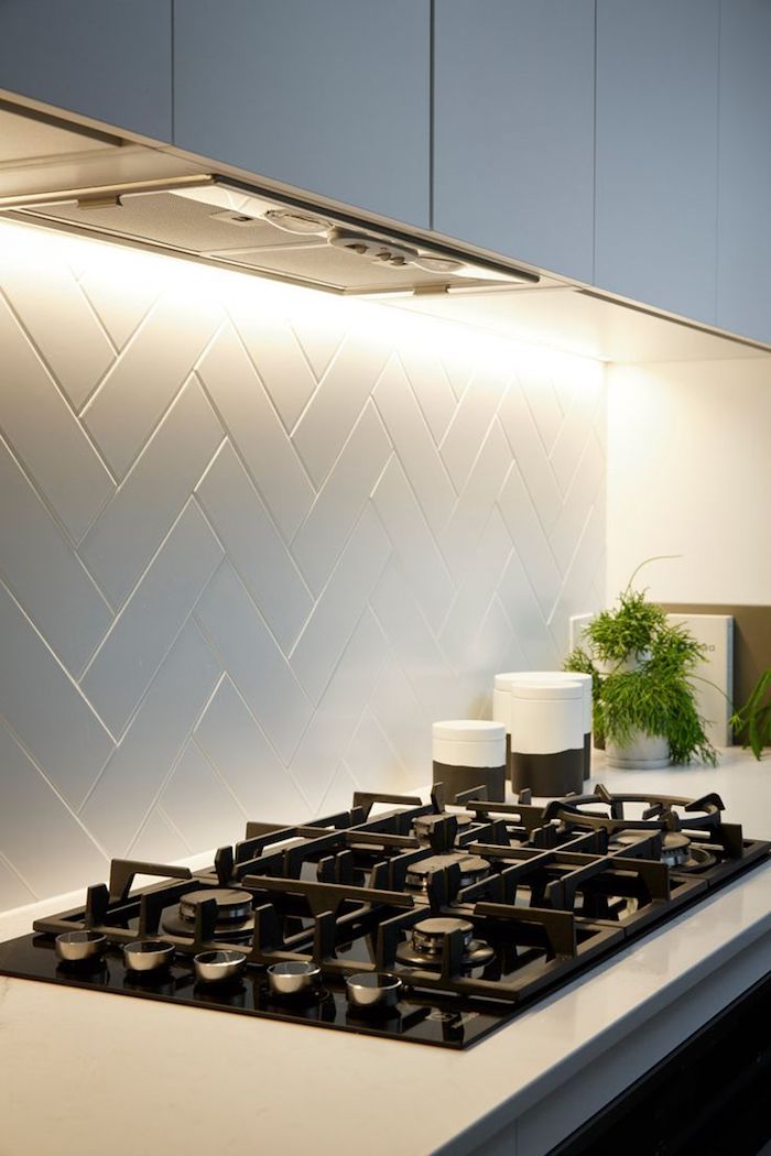 hob with a black surface, inbuilt in a white counter top, with a white herringbone backsplash, pale grey kitchen cabinets