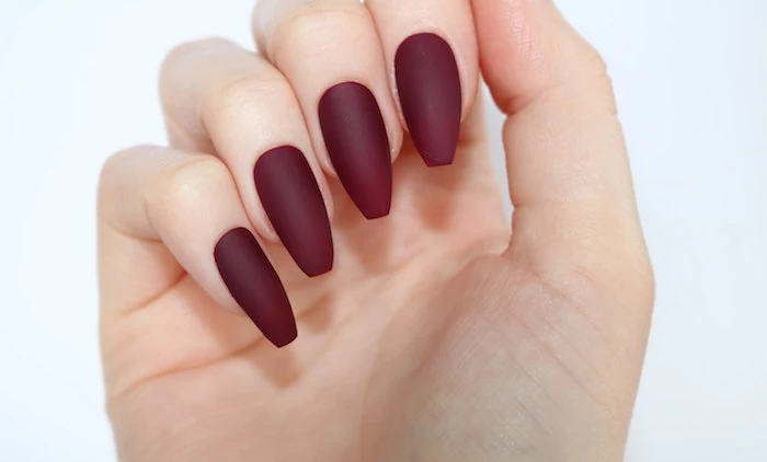 burgundy red matte coffin nails, attached to a pale hand, with folded fingers, seen in close up, on a plain white background