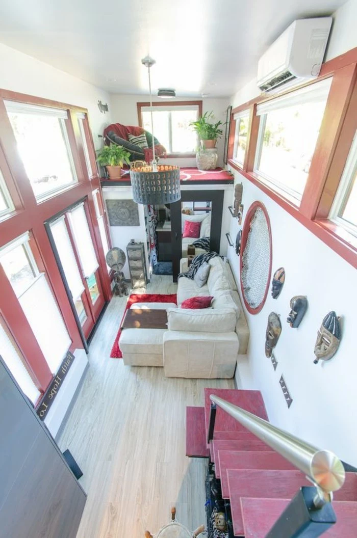 red accents inside a two story home, with a small beige corner sofa, living room furniture for small spaces, various decorations and potted plants, red armchair and several windows