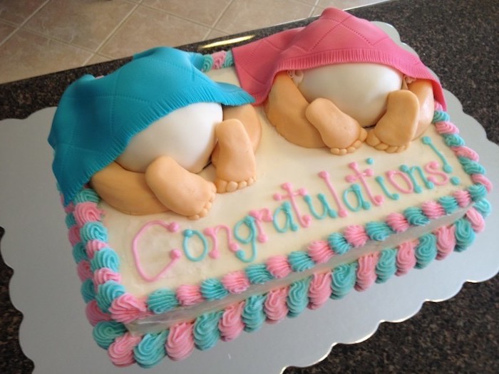 blankets in blue and pink, revealing two baby nappies and tiny legs, made from fondant, and decorating a white rectangular cake, baby shower sheet cakes, blue and pink frosting