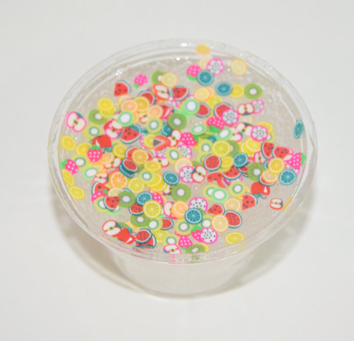 fruit stickers in the shapes of kiwi, apple and strawberry, orange and lime, watermelon and dragon fruit slices, and many others, decorating a tub of clear slime