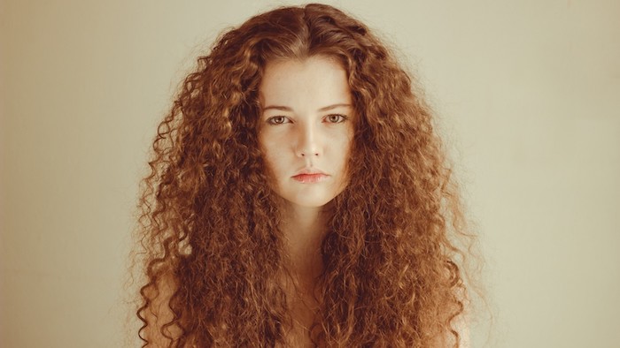serious-looking young woman, with long ginger or copper red hair, haircuts for curly hair, small dense curls, and middle part 