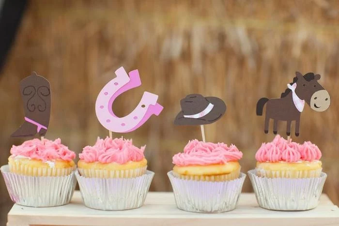 horse in brown, with pink bandana, brown cowboy hat, with pink ribbon, two pink horseshoes, and a brown cowboy boot, with pink spurs, baby shower cake toppers girl, on four pink cupcakes