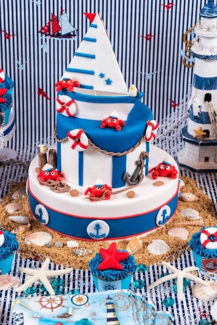 starfish and seashells, strewn around a white and blue cake, decorated with little red sailor crabs, and a small sailing boat, nautical baby shower cakes, various sea-related items 