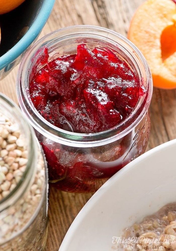 easy breakfast recipes, close up of a small clear glass jar, containing cranberry sauce, near a white bowl, and a larger jar with buckwheat