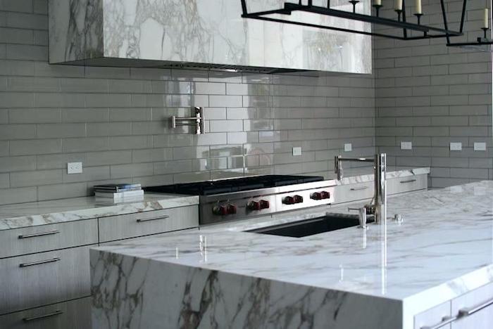 glossy grey subway tile kitchen backsplash, inside a room with marble counter tops, two metal stoves, and pale grey cabinets