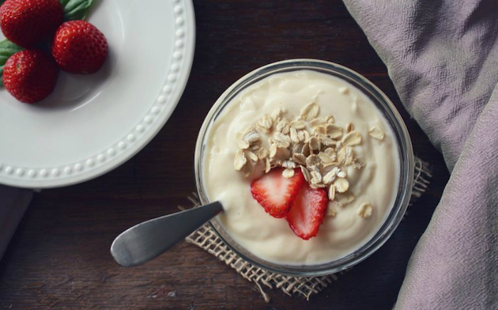 rolled oats and a halved strawberry, topping some creamy yoghurt, simple breakfast ideas, inside a glass dish, also containing a metal spoon