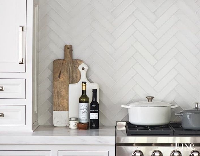 two cooking pots, on the black hob of a stove, near a marble counter top, with two cutting boards, two bottles and a small jar, white kitchen backsplash, with a herringbone pattern