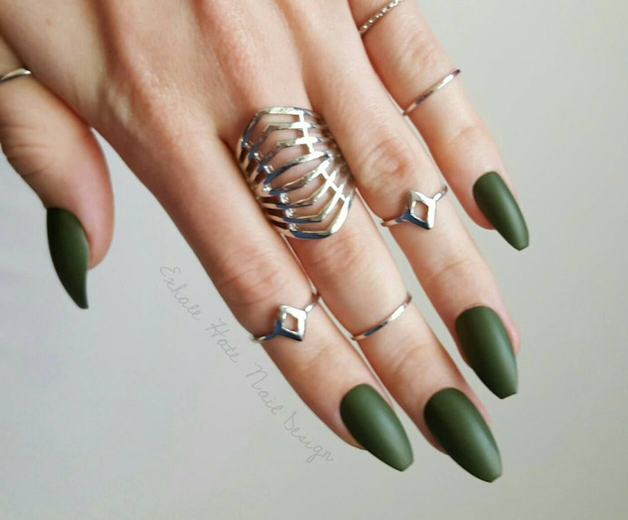 forest green matte nail polish, on a hand with medium long, coffin-shaped manicure, wearing seven different silver rings