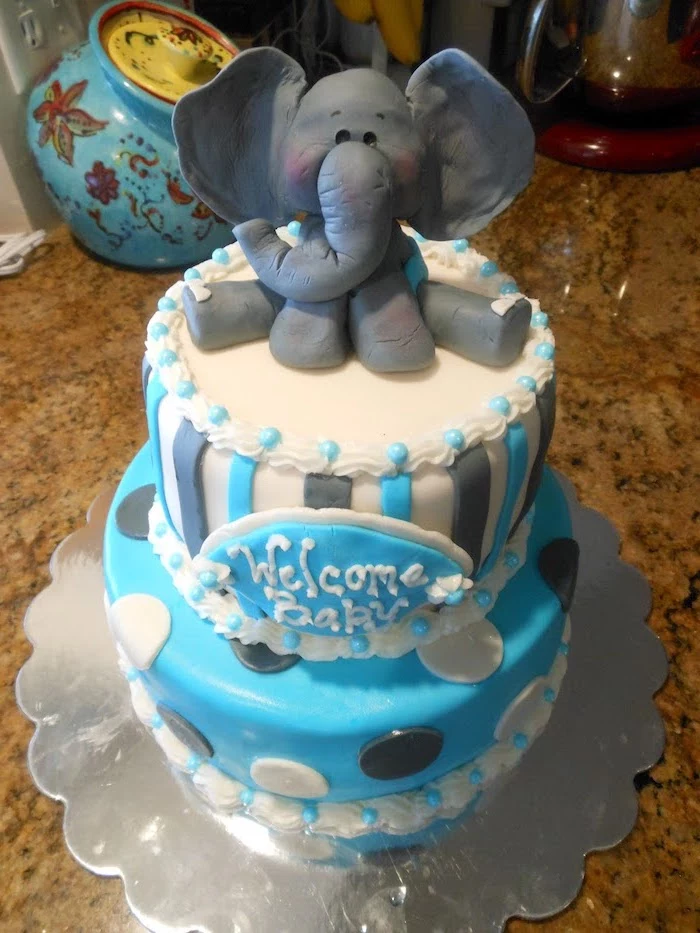 figurine of a baby elephant, made from dark grey fondant, topping a two-layer cake, in pale blue and white, with grey and white polka dots and stripes