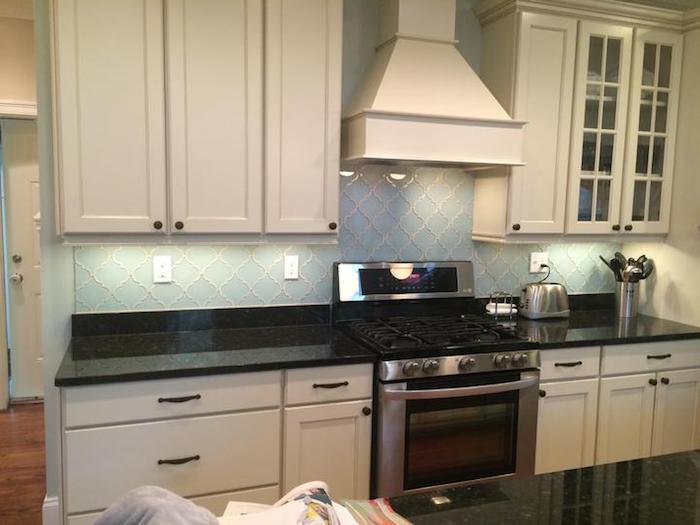 baby blue arabesque backsplash, with white joints, near white kitchen cabinets and drawers, smooth black counter top