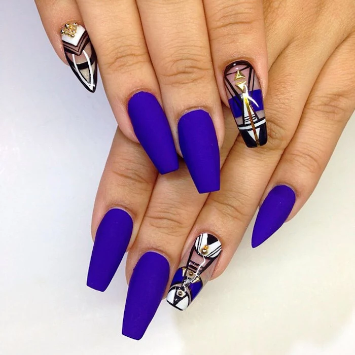 eight long coffin shaped nails, on two hands, placed on a white surface, five of the nails are painted in a vivid violet, matte nail polish, the other three are clear, and decorated with geometric motifs, and gold rhinestones