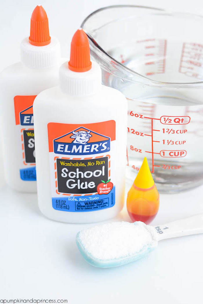 bottles of glue, near a plastic measuring spoon, filled with white powder, a tiny orange bottle, and a clear glass measuring jug, elmer's glue slime
