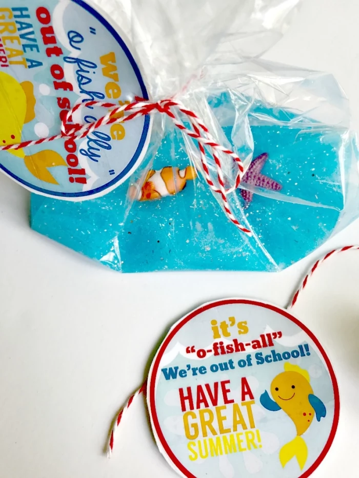 labels with colorful writing, and a drawing of a cartoon fish, tied to a clear plastic bag, containing ocean-inspired slime, how to make slime with shaving cream, glitter and tiny plastic fish ornaments